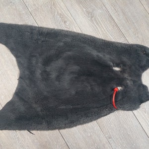 May include: A dark gray sheepskin rug with a hole in the center. The rug is laid out flat on a wooden floor.