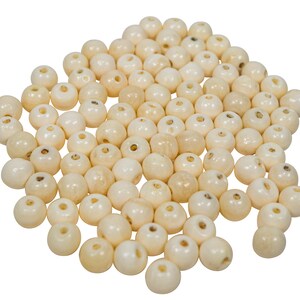 May include: A pile of off-white round beads with small holes in the center. The beads are made of bone or ivory.