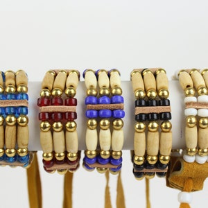 May include: Five beaded bracelets with wooden beads, gold beads, and colored glass beads. Each bracelet has a leather strap and a tassel.