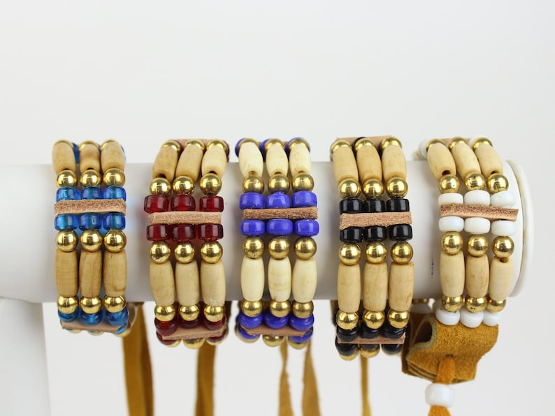 May include: Five beaded bracelets with wooden beads, gold beads, and colored glass beads. Each bracelet has a leather strap and a tassel.