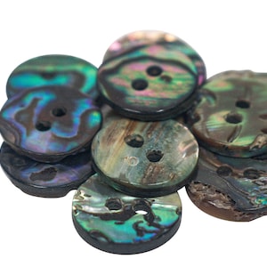 May include: A group of eight iridescent abalone shell buttons with two holes each. The buttons are various shades of green, blue, and brown.