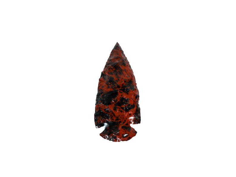 May include: A red and black arrowhead made of stone. The arrowhead has a pointed tip and a wide base.