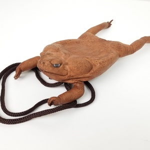 May include: A brown leather toad purse with a brown cord strap. The purse is shaped like a toad with a textured surface.
