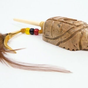 May include: A carved stone pipe with a wooden stem and a feather and bead embellishment. The pipe is shaped like a turtle and has intricate carvings.