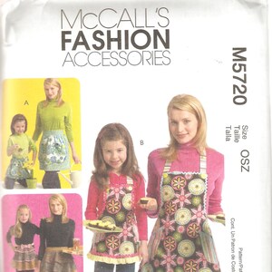 May include: A McCall's Fashion Accessories sewing pattern, M5720, featuring aprons. The cover shows women and children wearing aprons with floral and geometric designs. The aprons have pockets and decorative trim.