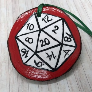 May include: A red wooden ornament with a white 20-sided die painted on it. The die has numbers 1 through 20 on its faces.