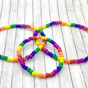 May include: Three rainbow colored beaded bracelets, each with a different size. The bracelets are made with small, round beads in the colors of the rainbow, with a purple bead at the end of each bracelet.