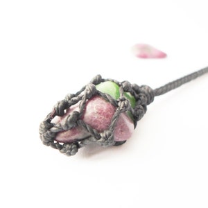 May include: A pink and green gemstone is wrapped in a black cord, creating a pendant. The cord is knotted in a decorative pattern.
