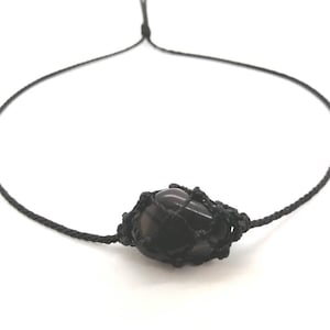 Op de afbeelding: Een zwarte edelsteen ketting met een zwarte koord. De edelsteen is gewikkeld in een zwarte macrame knoop.