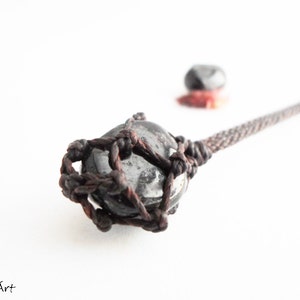 May include: A black and white stone pendant with a brown leather cord. The stone is wrapped in a knotted leather cord.