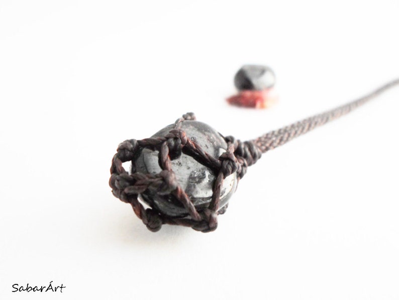 May include: A black and white stone pendant with a brown leather cord. The stone is wrapped in a knotted leather cord.