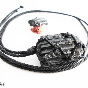 May include: Black Tourmaline crystal pendant necklace with a black cord. The crystal is wrapped in a black cord net.