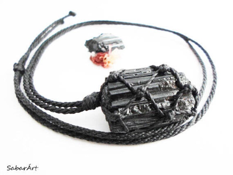 May include: Black Tourmaline crystal pendant necklace with a black cord. The crystal is wrapped in a black cord net.
