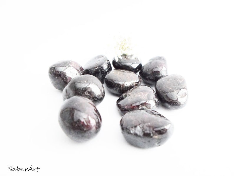 May include: A group of ten smooth, dark red and black tumbled stones. The stones are arranged in a cluster on a white background.