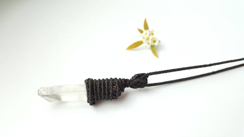May include: A clear quartz crystal pendant on a black cord necklace. The crystal is wrapped in black cord and tied with a knot.