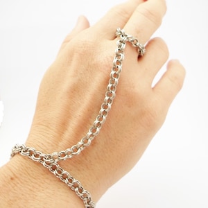 May include: A silver chain bracelet and ring set. The bracelet is worn on the wrist and the ring is worn on the index finger. The chain is made of small, interconnected links.