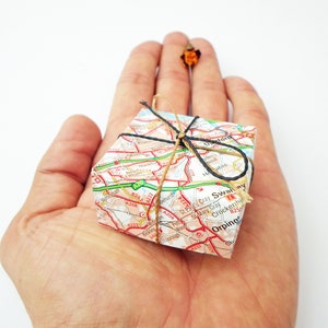 May include: A small gift box wrapped in a map of a city. The box is tied with twine and a black ribbon.