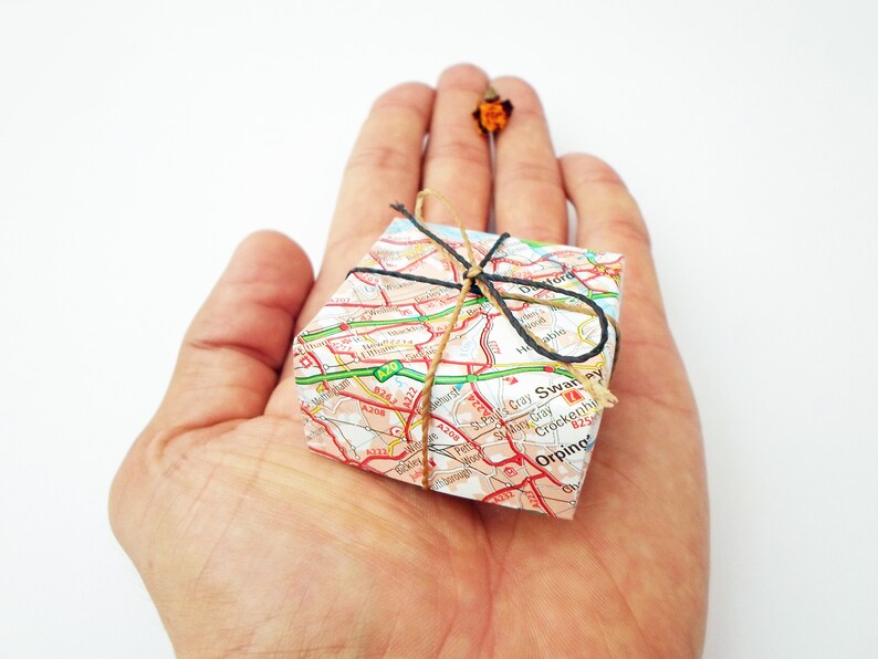 May include: A small gift box wrapped in a map of a city. The box is tied with twine and a black ribbon.