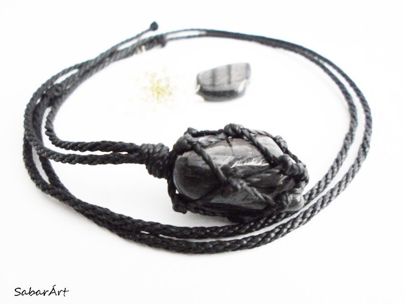 May include: Black gemstone pendant necklace with a black cord. The gemstone is wrapped in a black macrame knot.