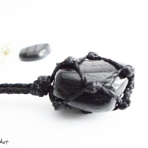 May include: Black gemstone pendant necklace with a black cord. The gemstone is wrapped in a black macrame knot design.