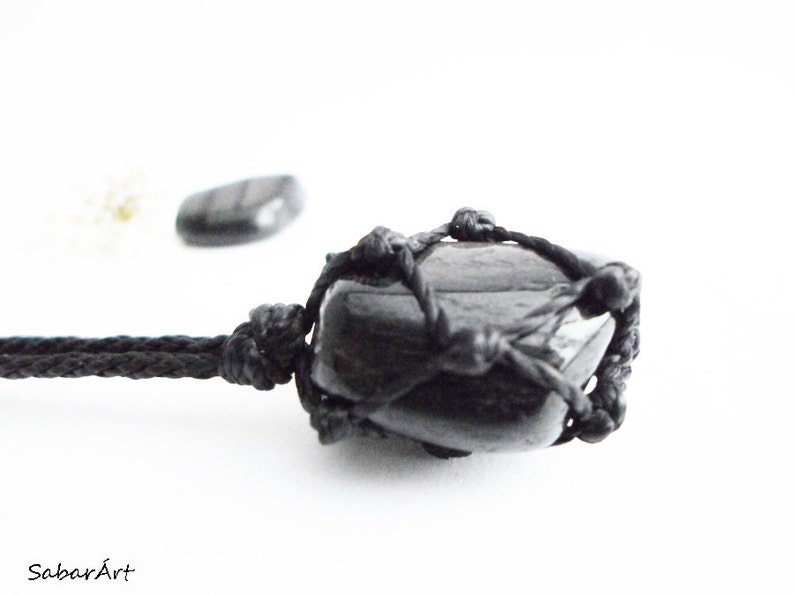 May include: Black gemstone pendant necklace with a black cord. The gemstone is wrapped in a black macrame knot design.