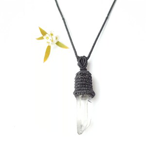 May include: A black cord necklace with a clear quartz crystal pendant wrapped in black cord. The pendant is shaped like a teardrop.