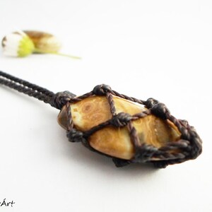Op de afbeelding: Een hanger van bruin en wit agaat, gewikkeld in bruin koord, hangend aan een bruin koord ketting.