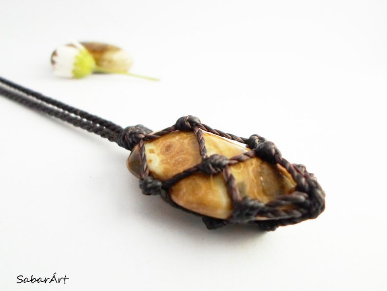 Op de afbeelding: Een hanger van bruin en wit agaat, gewikkeld in bruin koord, hangend aan een bruin koord ketting.