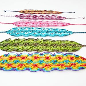May include: Six colorful macrame bracelets in various colors, including brown, pink, turquoise, green, and rainbow. Each bracelet features a woven design with a knotted pattern and long, thin cords extending from each end.