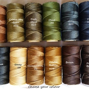 May include: A collection of 12 spools of embroidery floss in various colors, including brown, green, olive, gray, blue, black, straw, cinnamon, gold, and white. Each spool has a label with the color name and a number.