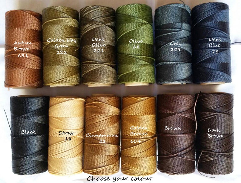 May include: A collection of 12 spools of embroidery floss in various colors, including brown, green, olive, gray, blue, black, straw, cinnamon, gold, and white. Each spool has a label with the color name and a number.