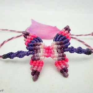 May include: A purple, pink, and white friendship bracelet with a butterfly knot design.