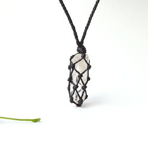 May include: A clear quartz crystal pendant in a black macrame knot necklace. The pendant is hanging from a black cord.