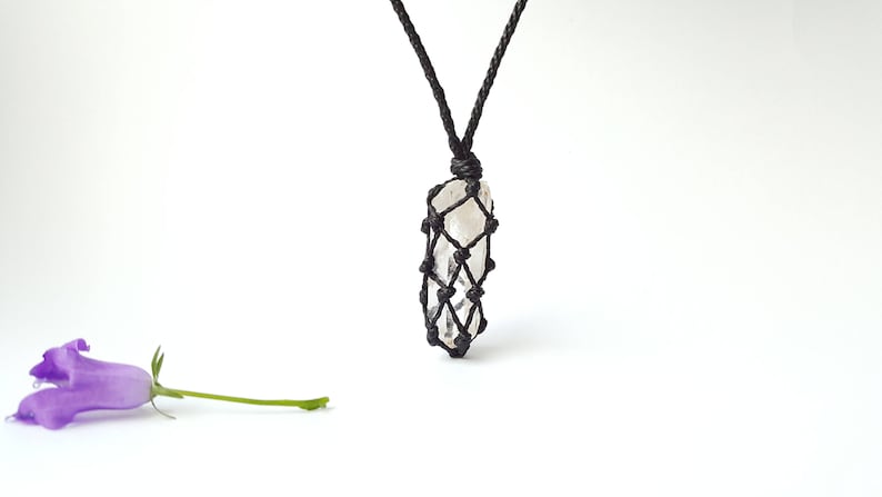 May include: A clear quartz crystal pendant in a black macrame knot necklace. The pendant is hanging from a black cord.