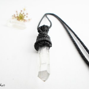 May include: A clear quartz crystal pendant with a black macrame knot, hanging from a black cord.