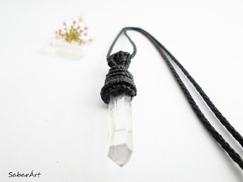 May include: A clear quartz crystal pendant with a black macrame knot, hanging from a black cord.