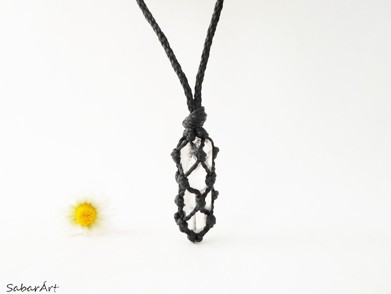 May include: A clear quartz crystal pendant hangs from a black cord. The crystal is wrapped in a macrame knot design.