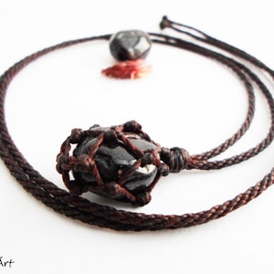 May include: A black gemstone pendant necklace with a brown cord. The gemstone is encased in a knotted macrame design.