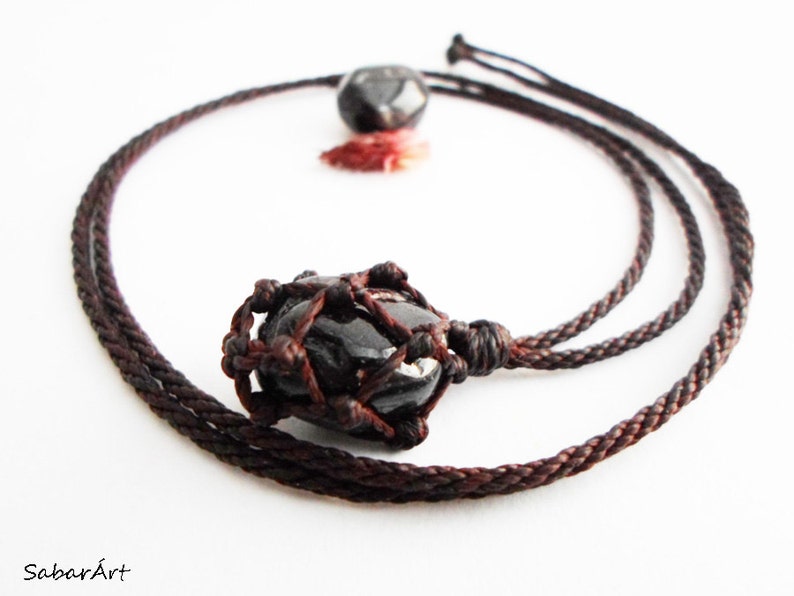 May include: A black gemstone pendant necklace with a brown cord. The gemstone is encased in a knotted macrame design.