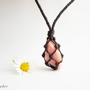 May include: A pink opal gemstone pendant necklace with a brown macrame cord. The pendant is tied in a knot with a diamond shape.