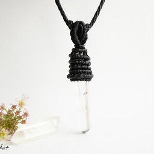 May include: A clear quartz crystal pendant on a black cord necklace. The cord is knotted into a decorative design at the top of the pendant.