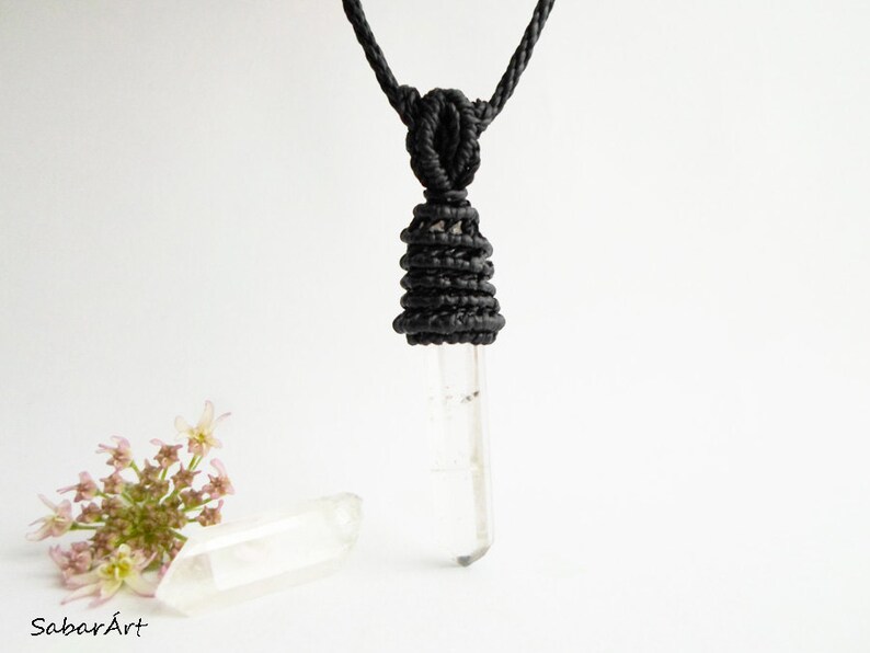 May include: A clear quartz crystal pendant on a black cord necklace. The cord is knotted into a decorative design at the top of the pendant.