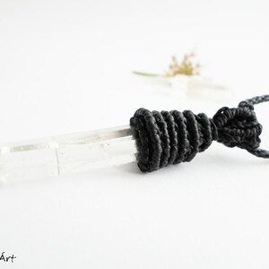 May include: A clear quartz crystal pendant with a black cord and a black macrame knot.
