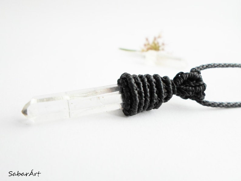 May include: A clear quartz crystal pendant with a black cord and a black macrame knot.