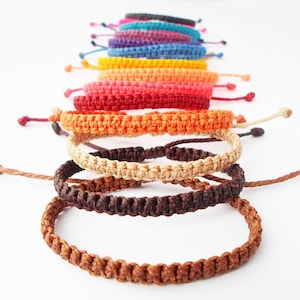 Può includere: Un mucchio di braccialetti intrecciati colorati in varie tonalità di rosso, arancione, giallo, verde, blu, viola e marrone.