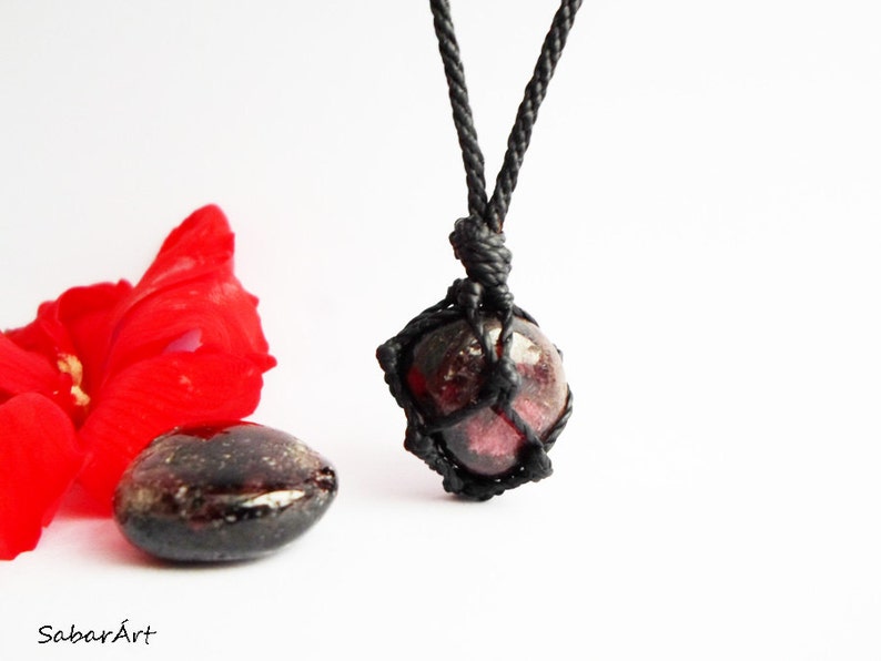 May include: A dark red gemstone pendant necklace with a black cord. The gemstone is wrapped in a black cord macrame knot.