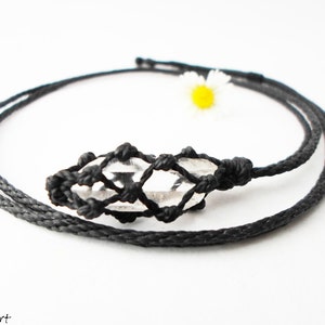 May include: A clear quartz crystal pendant in a black macrame knot necklace. The necklace is made with black cord and has a simple design.