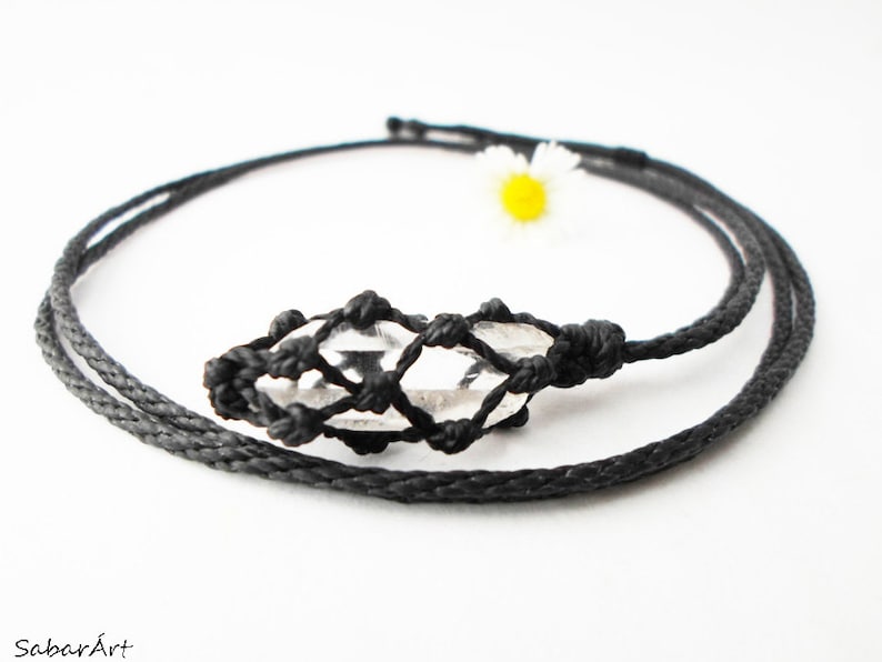 May include: A clear quartz crystal pendant in a black macrame knot necklace. The necklace is made with black cord and has a simple design.
