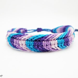 May include: A braided friendship bracelet with a blue, purple, and pink color scheme. The bracelet is made with a woven cord and has a simple knot closure.