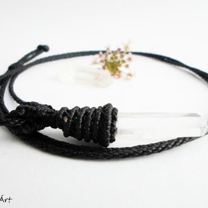 May include: A clear quartz crystal pendant on a black cord necklace. The cord is tied with a knot at the top of the pendant.